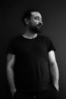Captivating black and white portrait of a man with a beard and black T-shirt, hands in pockets.