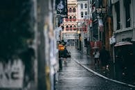 雨中的小巷里，人们撑着伞行走，城市景象以建筑物和标牌为特色