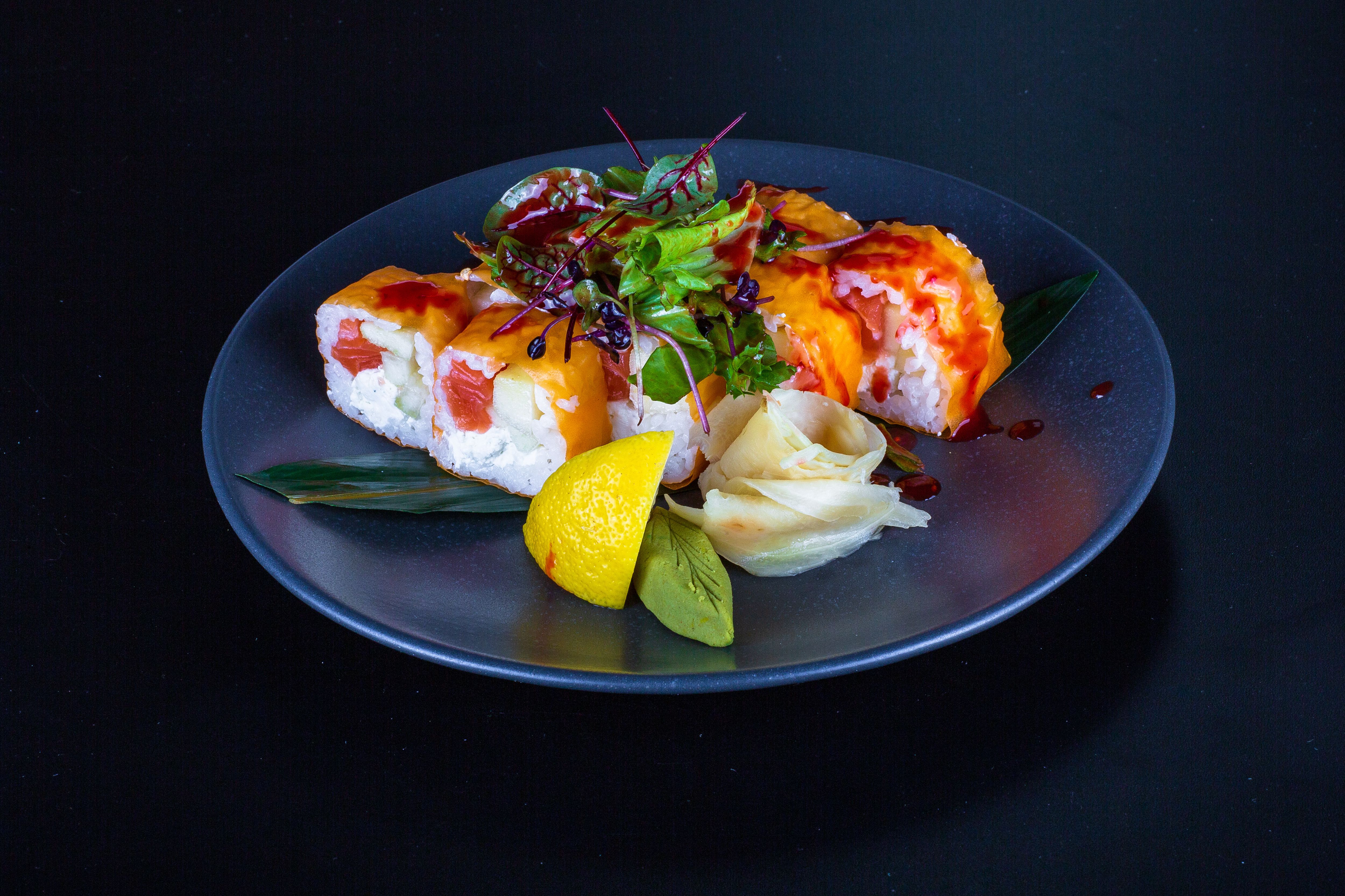 Vibrant sushi rolls served with salad, lemon, and ginger on a dark plate for a gourmet dining experience.