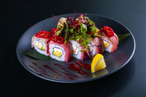 Free Exquisite sushi rolls with fresh greens, vibrant peppers, and lemon garnish on a black plate. Stock Photo