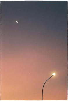 A tranquil evening scene showing a crescent moon and a lit street lamp against a colorful sky.