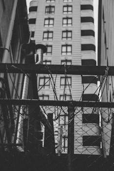 透过铁丝网栅栏，一座现代城市建筑以黑白色被捕捉下来