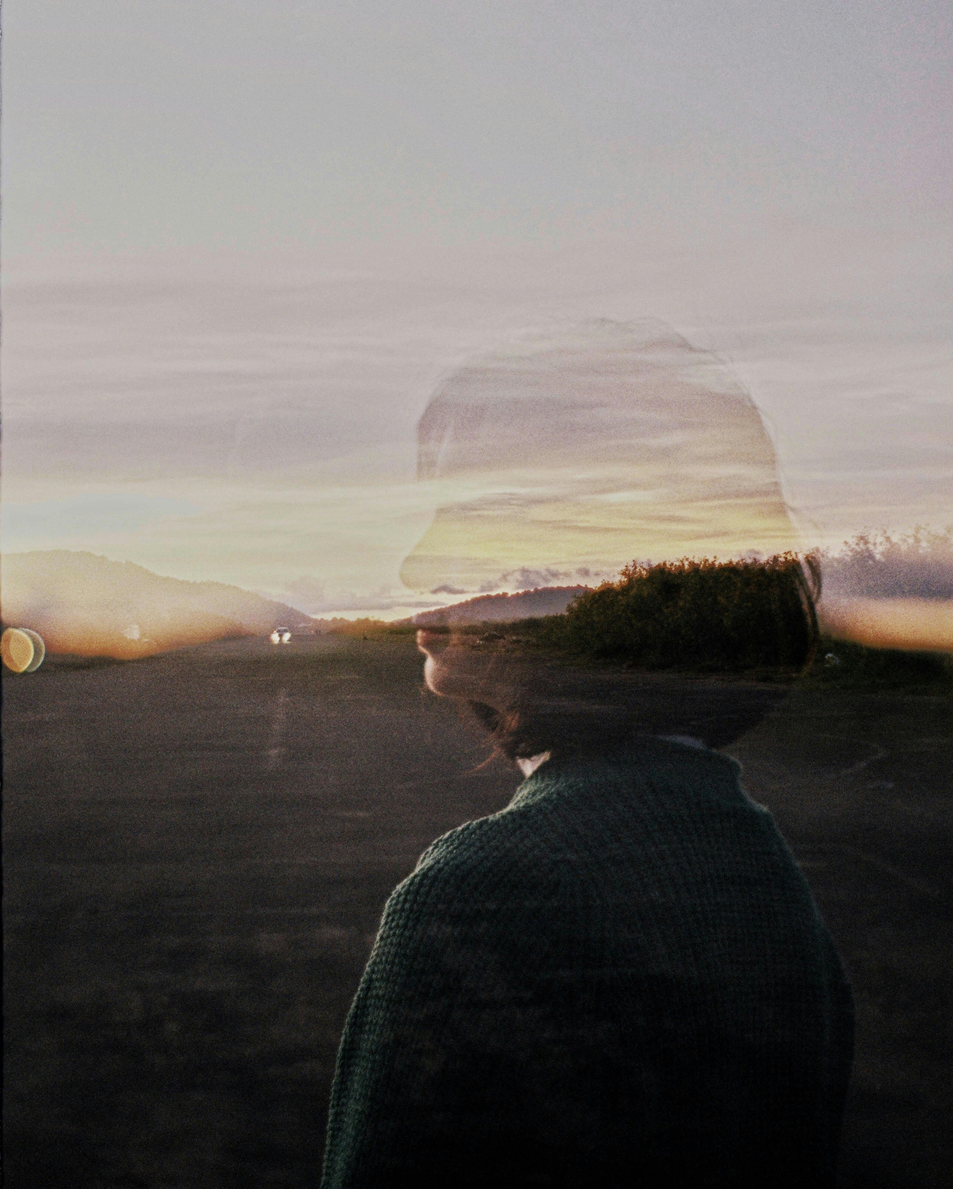 Artistic double exposure image of a woman's silhouette against a sunset landscape.