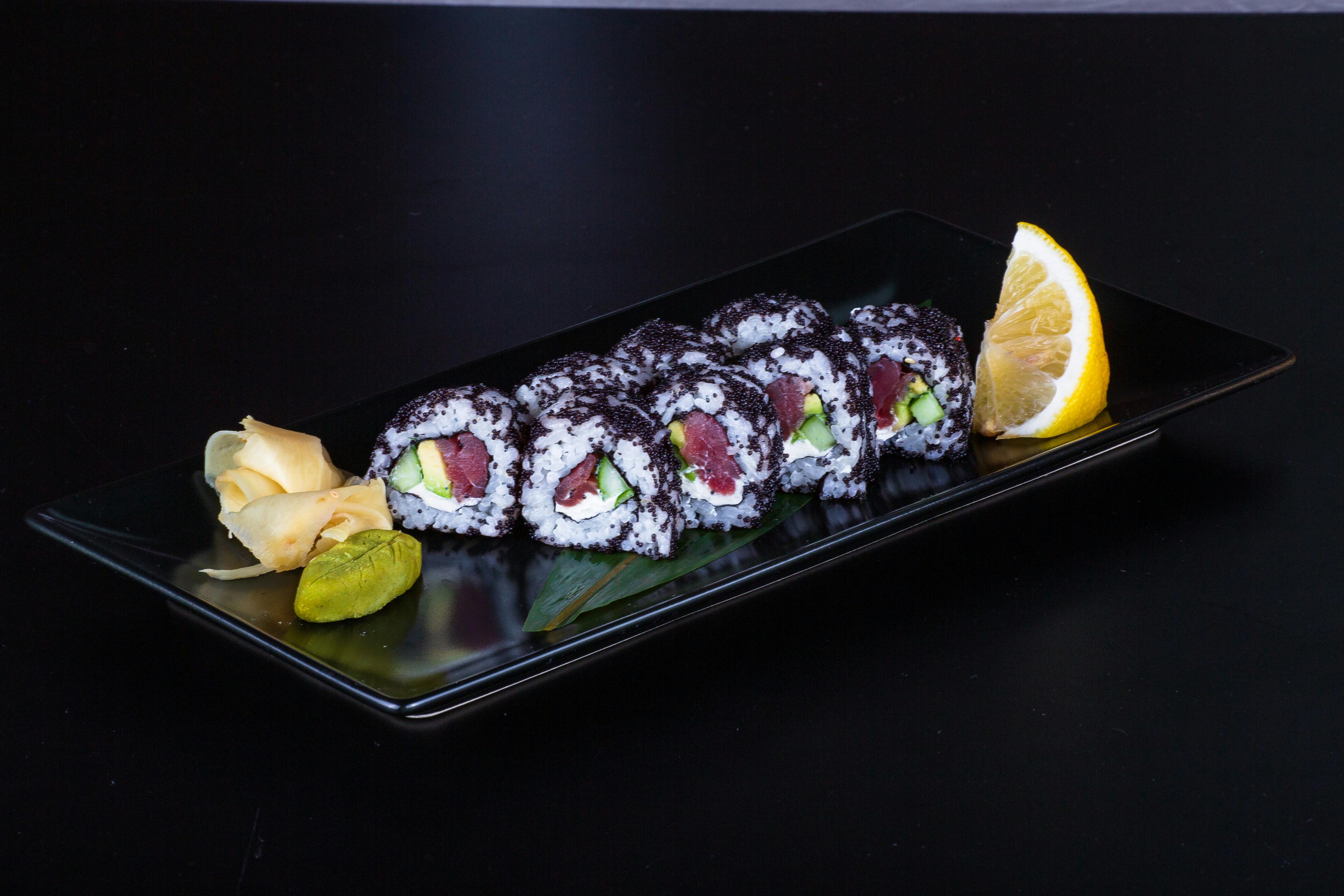 A black plate with sushi rolls and a lemon wedge · Free Stock Photo