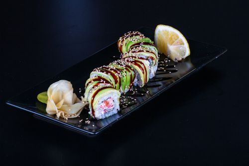 Free Mouthwatering sushi roll topped with avocado and sesame, garnished with ginger and lemon. Stock Photo