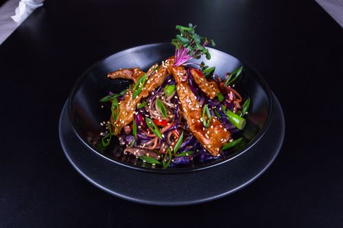 Free A delicious Asian stir fry with crispy sesame chicken, vegetables, and noodles in a black bowl. Stock Photo