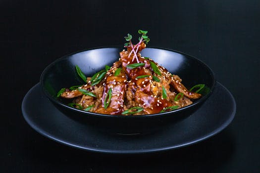 A flavorful Asian chicken dish served with rice, garnished with sesame seeds and spring onions.