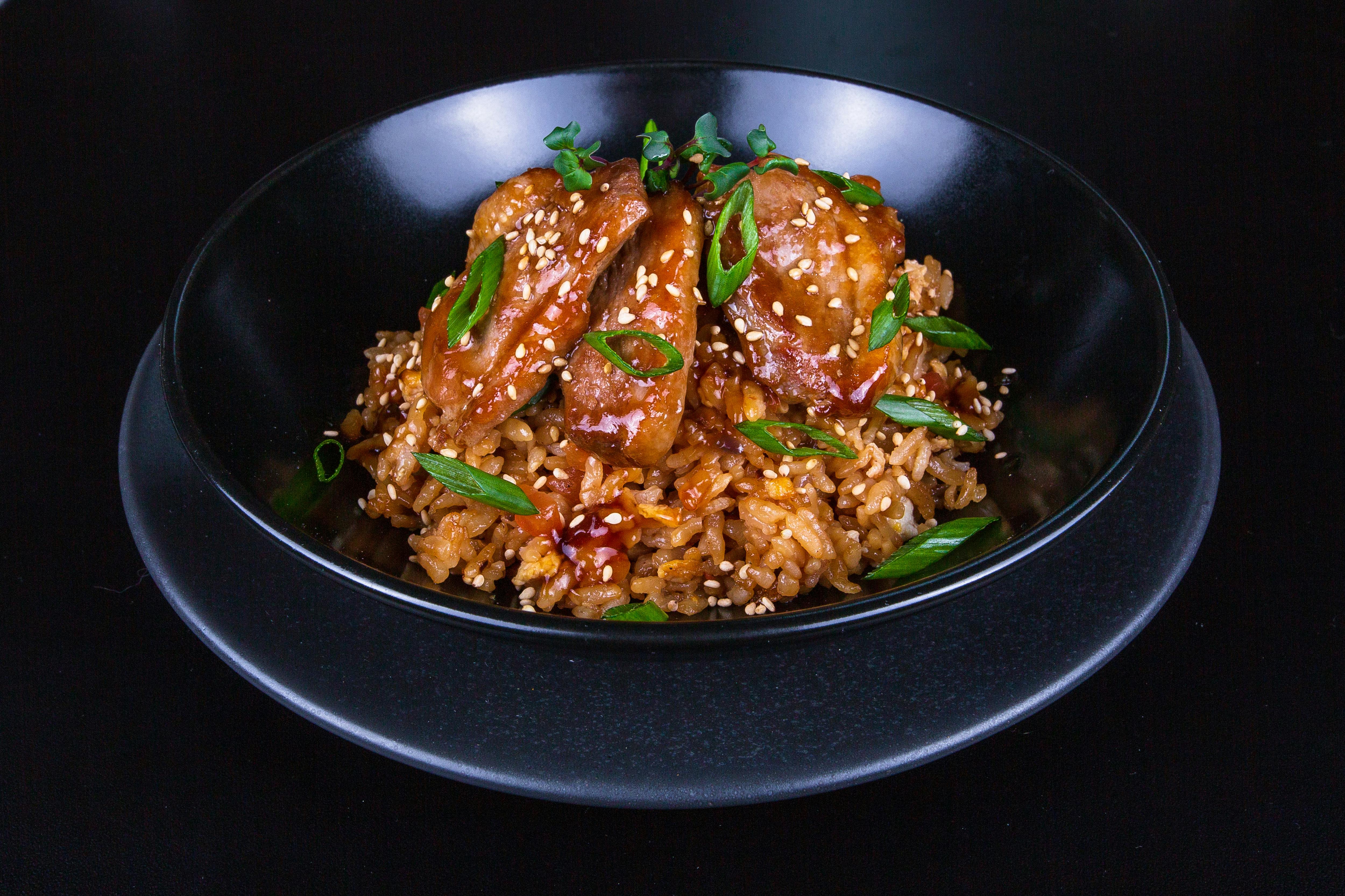 Close-up of a flavorful Asian chicken dish with rice and spring onions in a black bowl.