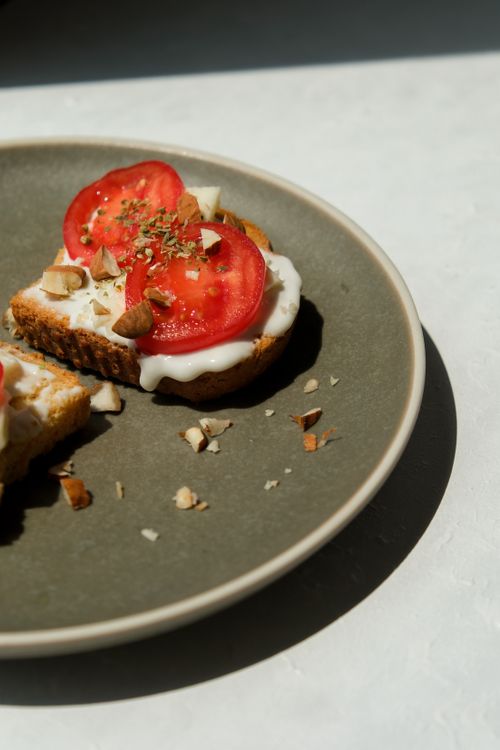 Free Close-up of tomato toast with cream cheese and nuts on a plate, perfect for breakfast. Stock Photo
