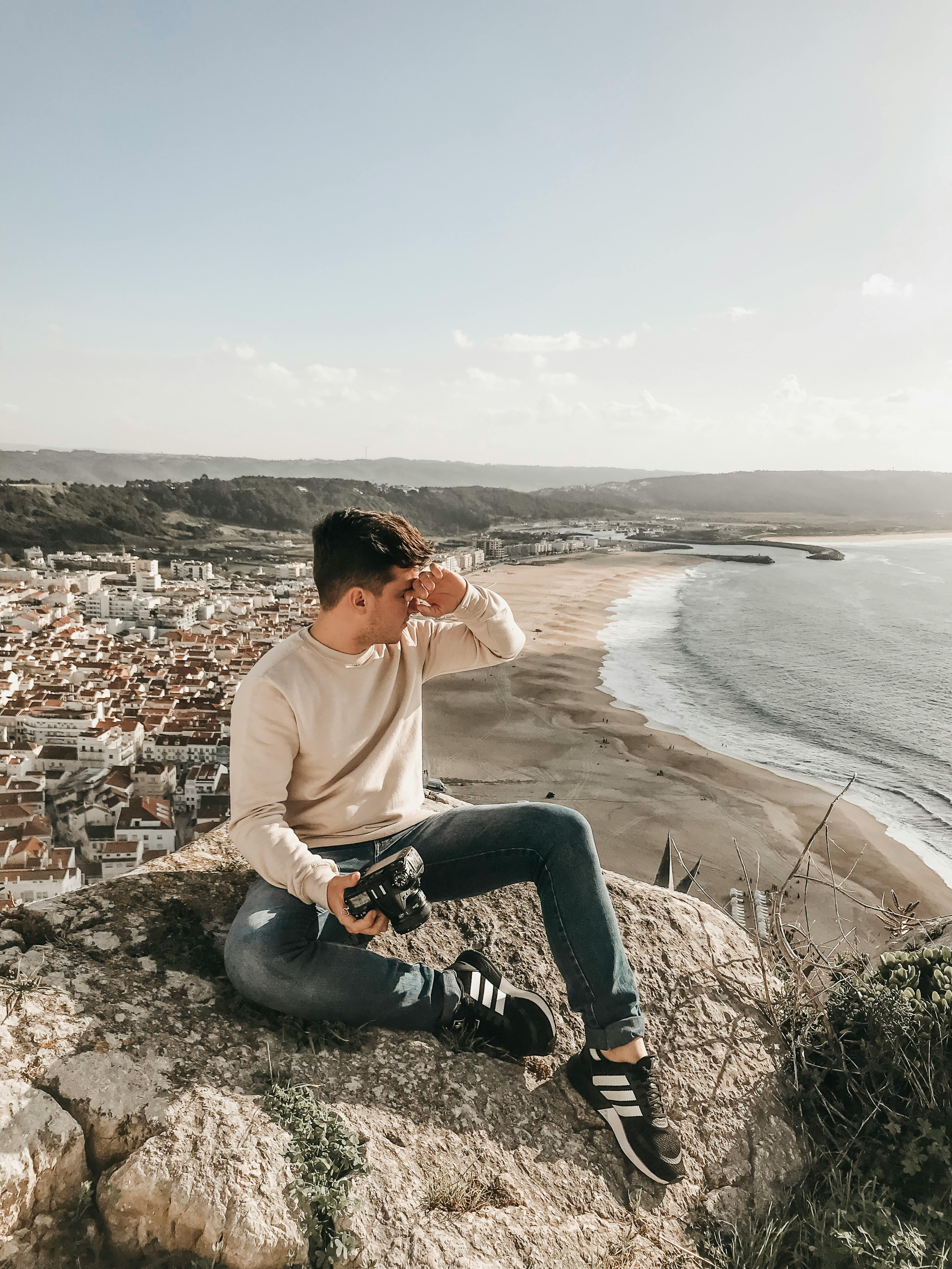 photographer holding dslr camera sitting on a huge rock