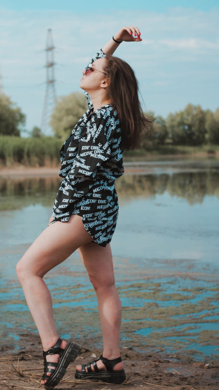 Young Woman In A Summer Outfit Standing Near A Body Of Water 