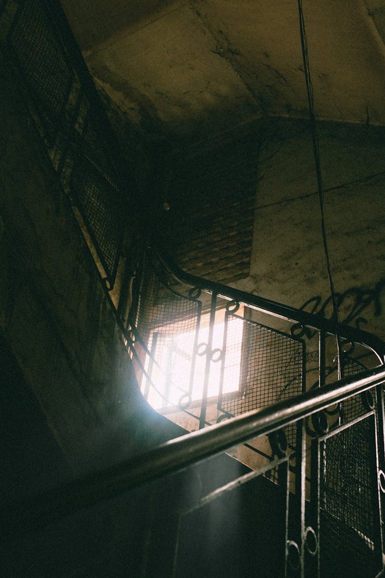 Dark Staircase With A Decorative Balustrade, And A Bright Light Coming From The Window