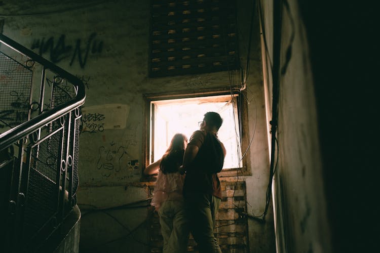 Couple Standing On A Dark Staircase By A Bright Window 