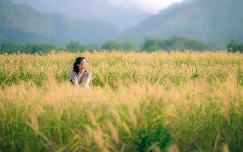 Free Young woman enjoying a peaceful moment amidst a lush summer field with mountains in the background. Stock Photo