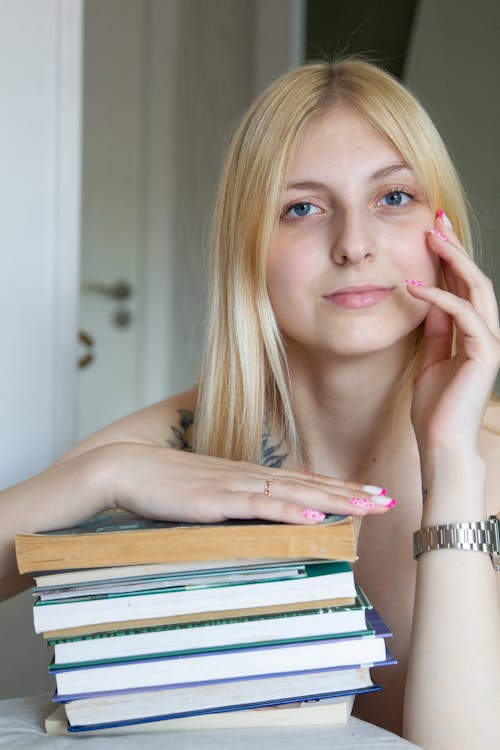 A blonde woman with long hair is sitting on a stack of books