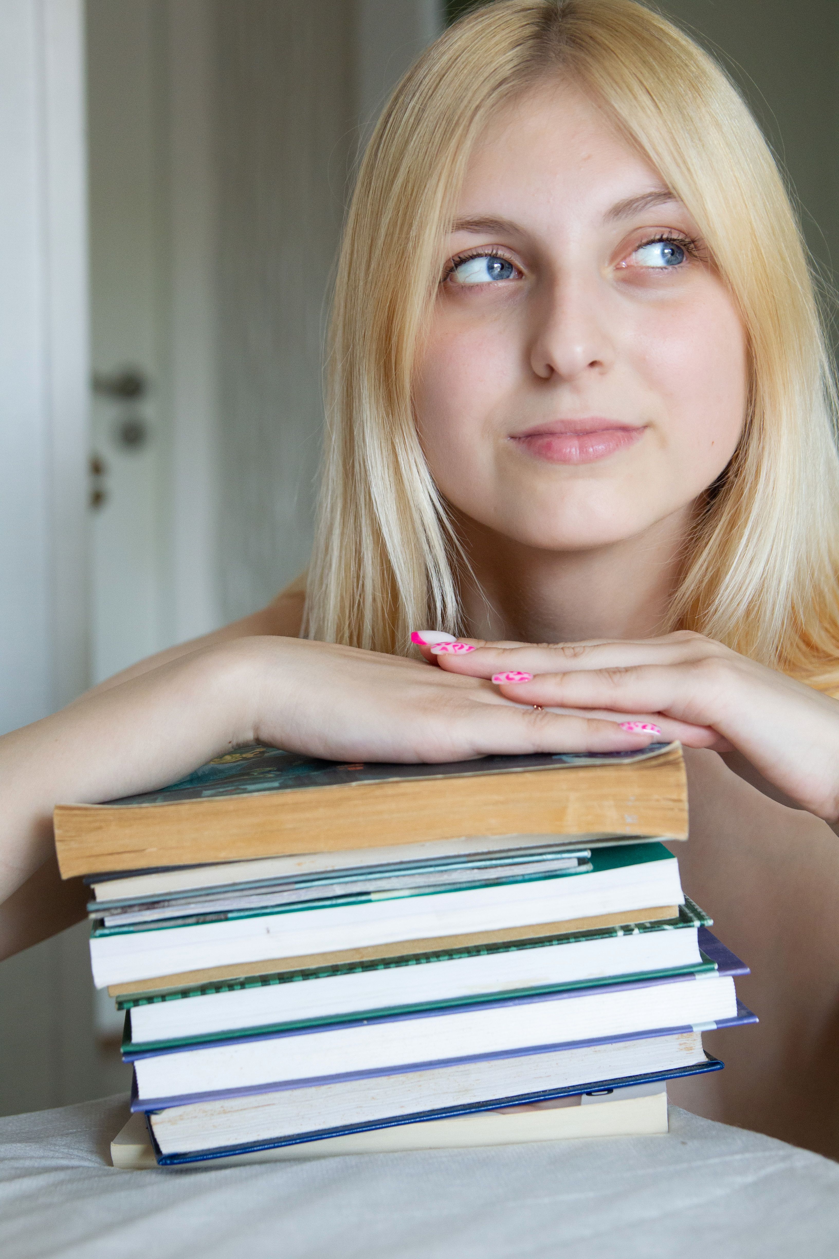 A young woman is holding a stack of books · Free Stock Photo