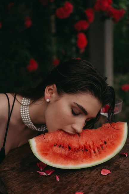 A young woman bites into a juicy watermelon slice in a vibrant outdoor setting.