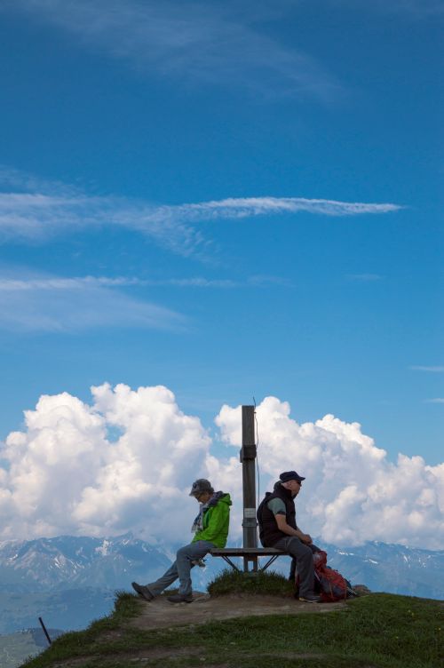 Free Two hikers resting on a bench atop a mountain with a beautiful alpine view in Switzerland. Stock Photo