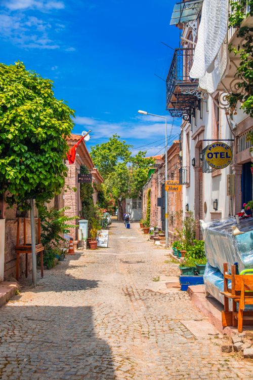Free Vibrant, sunlit cobblestone street in historic Ayvalık, Türkiye, showcasing traditional architecture. Stock Photo