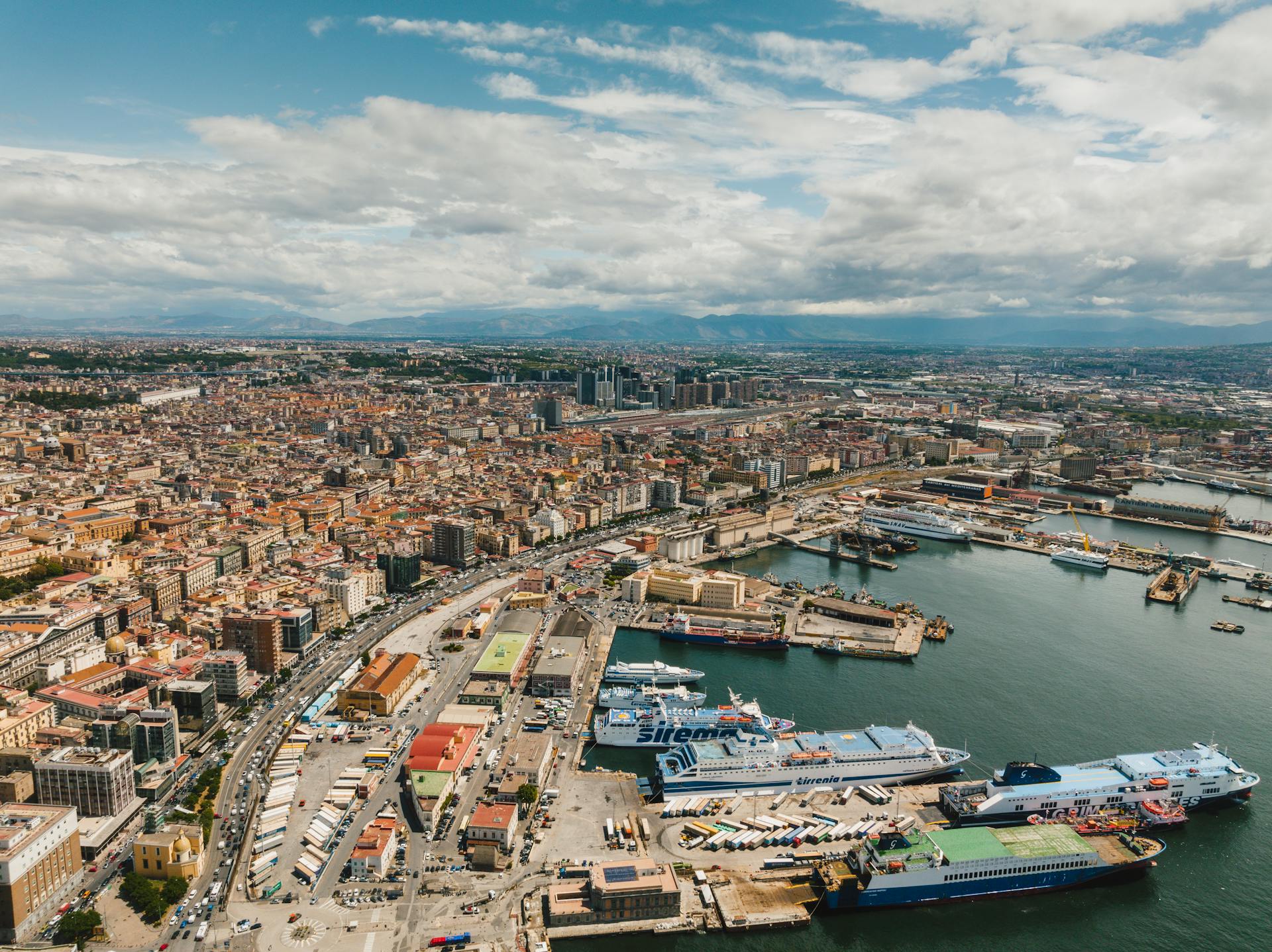 Captivating aerial view of Naples harbor with ships and cityscape under a cloudy sky.