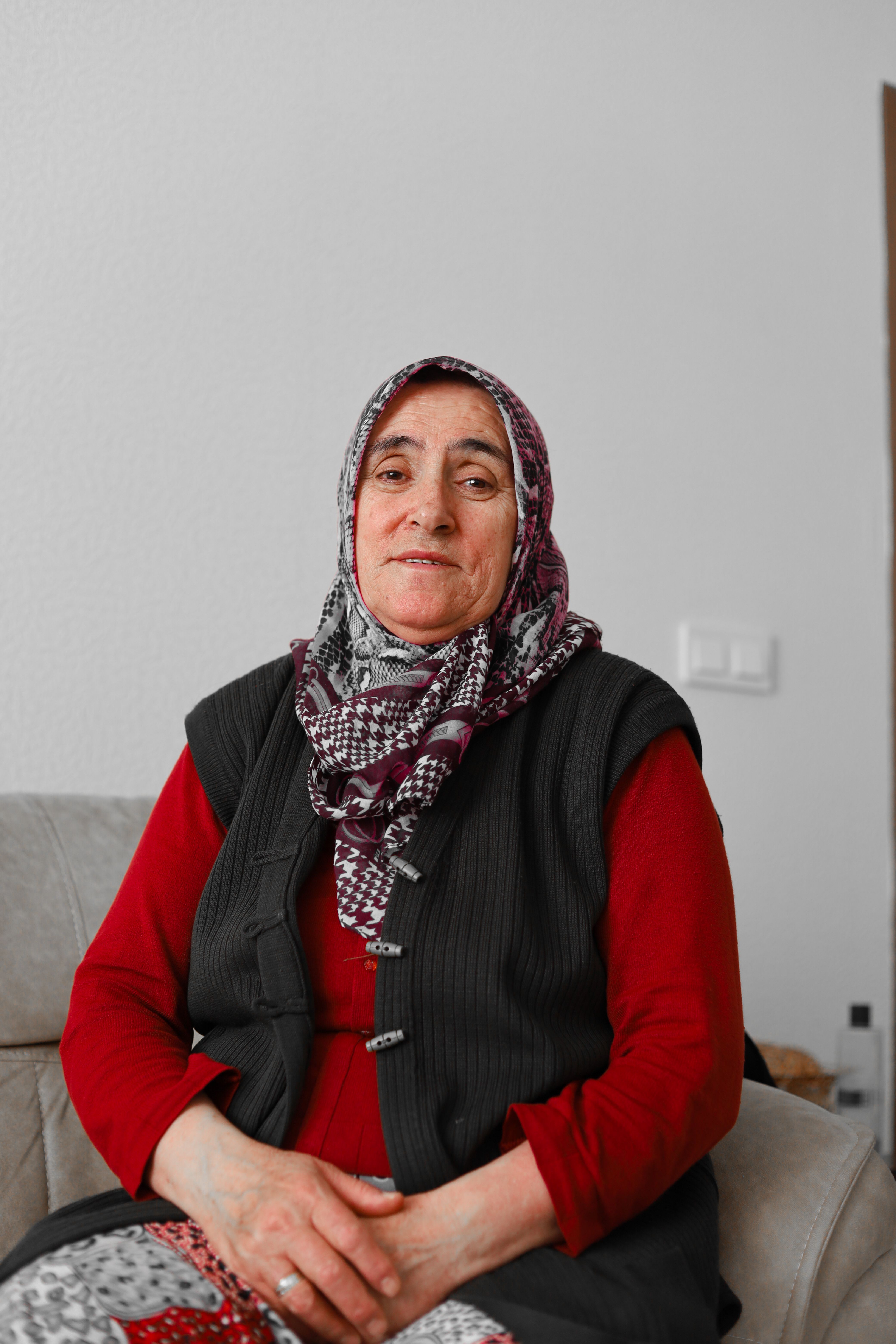 Elderly woman wearing a patterned headscarf, sitting indoors on a couch in Ankara, Türkiye.