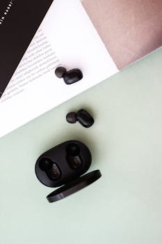 A minimalist flat lay showcasing black wireless earbuds on a pastel green background with an open book.