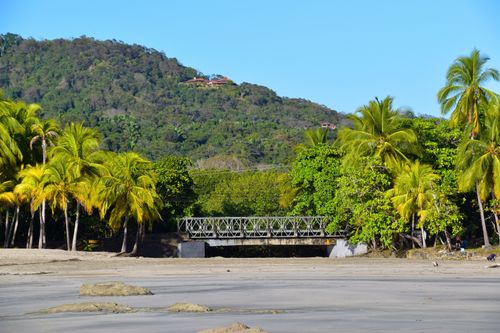 Free A scenic view of a tropical beach with a metal bridge and lush palm trees in the background. Stock Photo