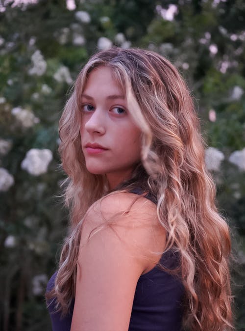 Young Woman with Wavy Blonde Hair Standing in a Garden 