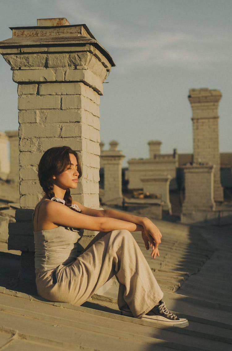 Woman Sitting On House Roof On Sunset