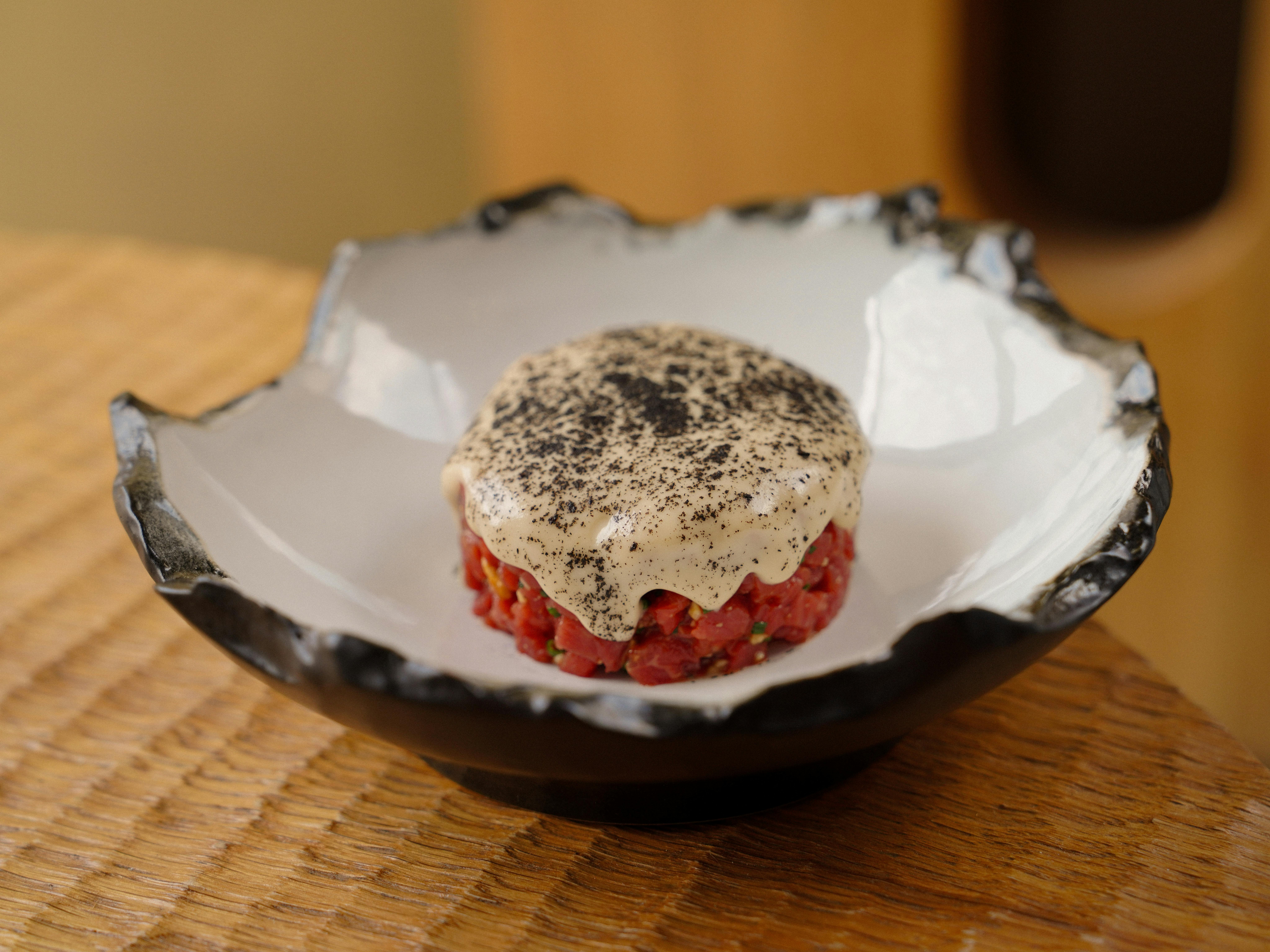 Close-up of gourmet steak tartare topped with a savory foam in a decorative bowl.