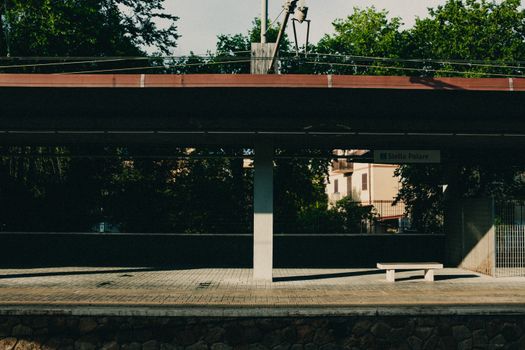 Empty train station platform at Stella Polare with green trees and sunlight casting shadows.