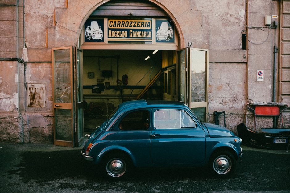A classic Fiat Cinquecento parked outside an Italian garage. Perfect vintage urban scene.