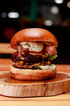 Mouthwatering gourmet burger with bacon and sauce served on a rustic wooden board, perfect for food lovers.