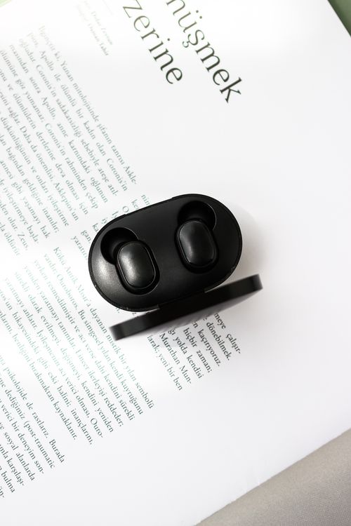 Free Black wireless earbuds placed on an open book, blending technology and literature. Stock Photo