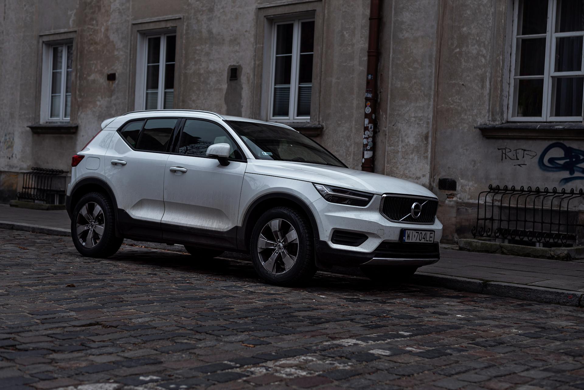 A white SUV Volvo XC40 parked on a cobblestone street in a European urban area, highlighting urban transportation.