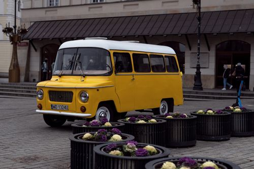 Free Classic yellow van parked on a European street, surrounded by vibrant flower pots and historic architecture. Stock Photo