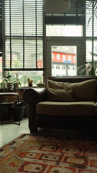 A stylish urban living room with a sofa, potted plants, and large windows.