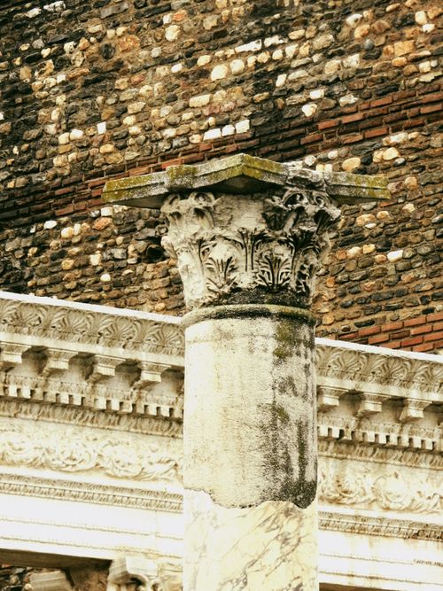 Free Detailed view of an ancient Roman column with ornate carvings against a textured brick wall. Stock Photo