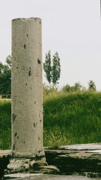 A solitary ancient stone column stands amidst grassy ruins, evoking historical wonder.