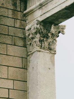 Close-up of an ornate ancient stone column capital beside a brick wall.