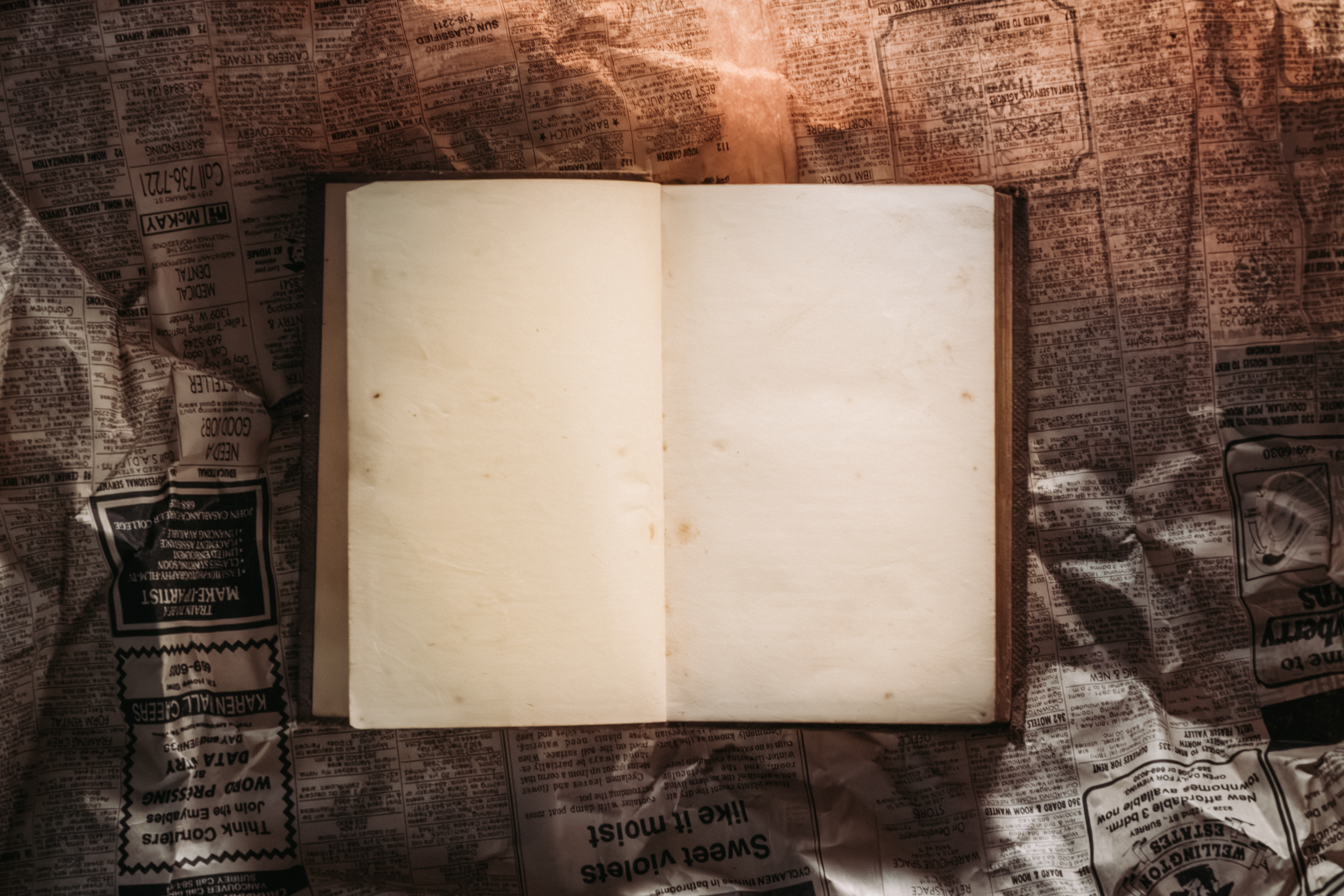 An open blank book placed on vintage crumpled newspapers, softly lit.
