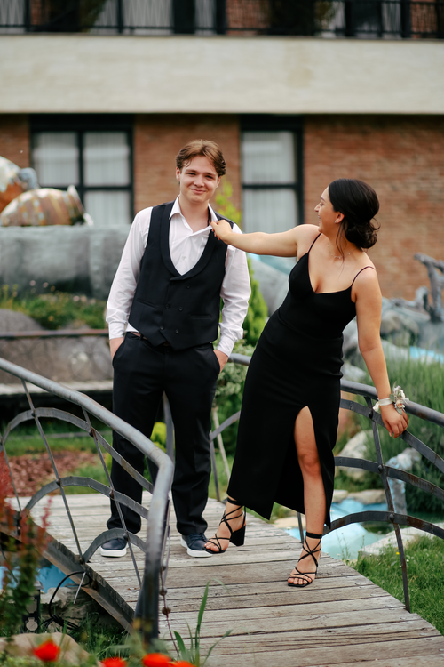 Free Smiling couple in formal attire pose on a picturesque wooden bridge at a park. Stock Photo