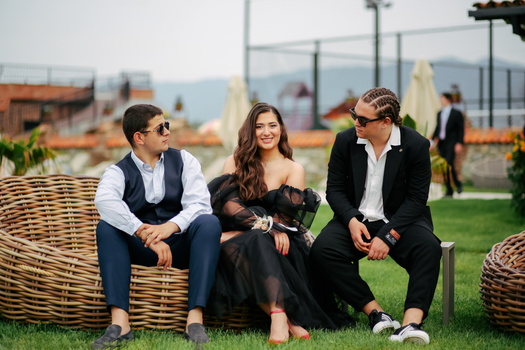 Group of three well-dressed individuals sitting outdoors at a wedding event.