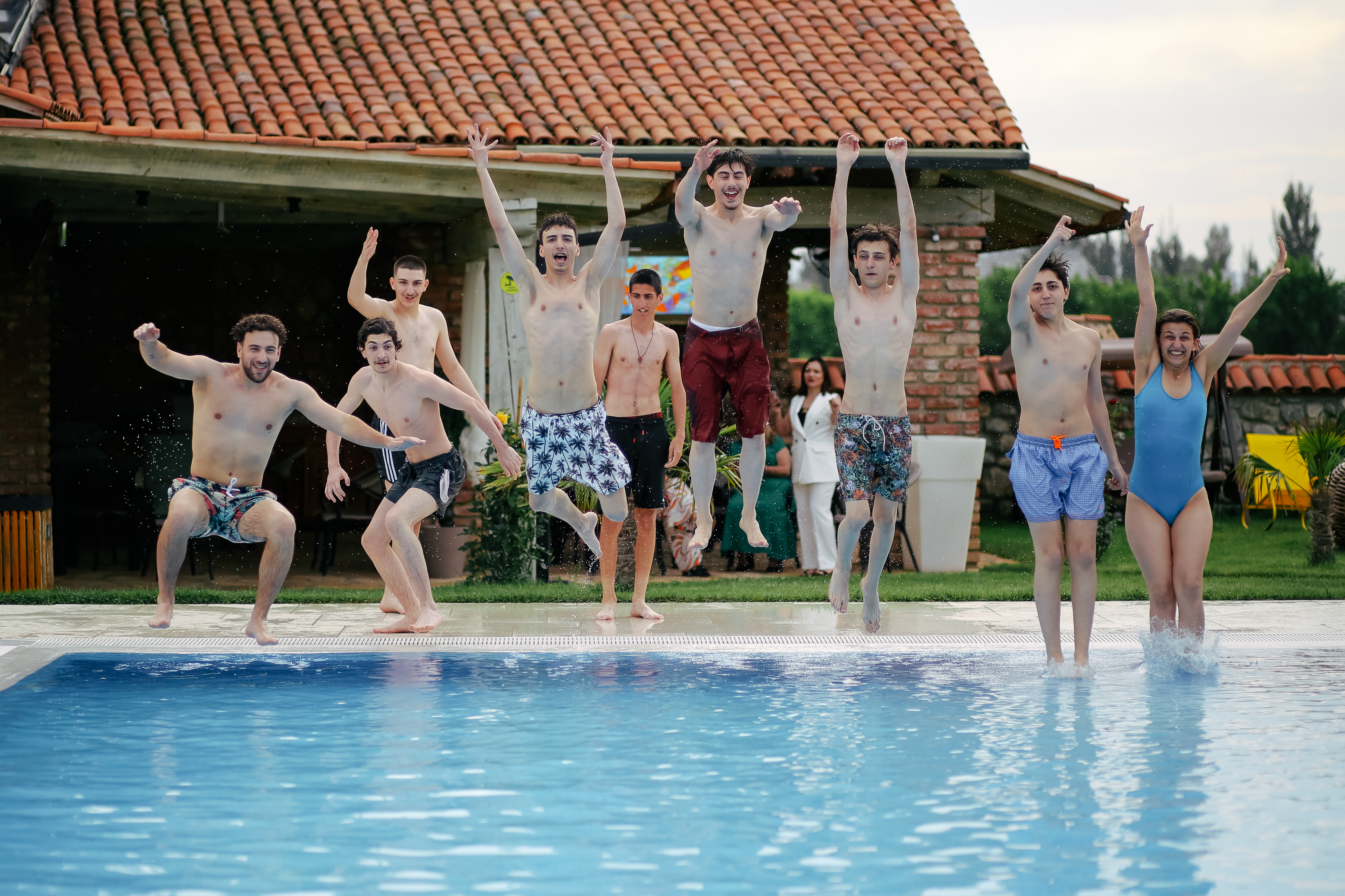 Young friends joyfully jumping into a pool, enjoying a sunny outdoor gathering.