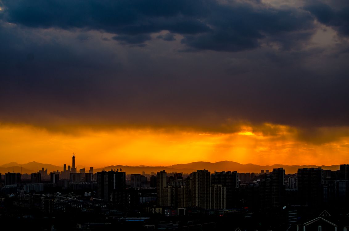 Free A breathtaking silhouette of a city skyline at sunset with vibrant clouds and a glowing horizon. Stock Photo