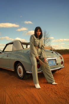 Fashionable woman leaning against a vintage convertible car in a desert setting. Stylish mood.