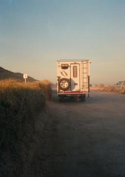 A van parked on a dirt road during sunset, with a clear sky and scenic landscape.