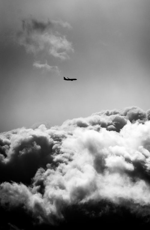 Free Silhouette of an airplane soaring over dramatic, cloudy skies in black and white, capturing the essence of travel and aviation. Stock Photo