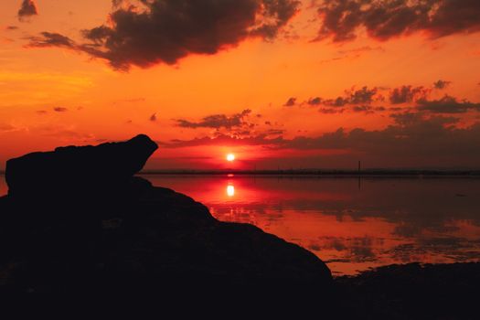 Stunning sunset over a calm lake with silhouetted rocks, vibrant sky reflections.
