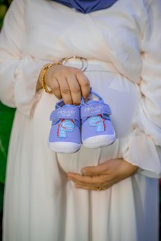 A close-up of a pregnant woman holding baby shoes, symbolizing motherhood and anticipation. - Fotografer Sidoarjo